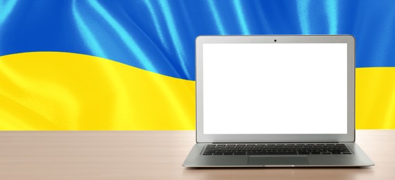 Laptop with blank screen on table and Ukrainian national flag on background, space for text. Banner design