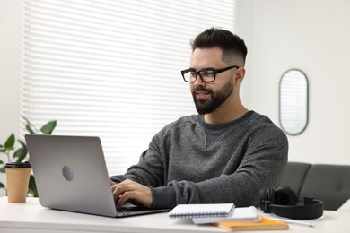 Photo of E-learning. Young man using laptop during online lesson at white table indoors