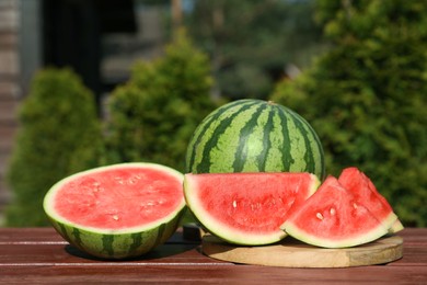 Photo of Delicious cut and whole ripe watermelons on wooden table outdoors