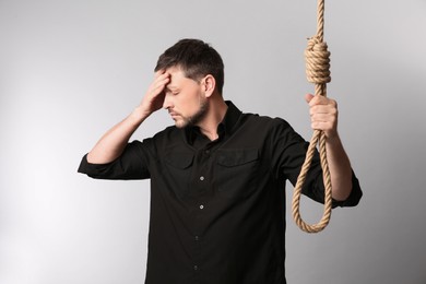 Photo of Depressed man with rope noose on light background