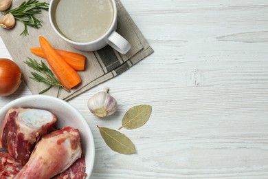 Photo of Mug with delicious bone broth and ingredients on white wooden table, flat lay. Space for text