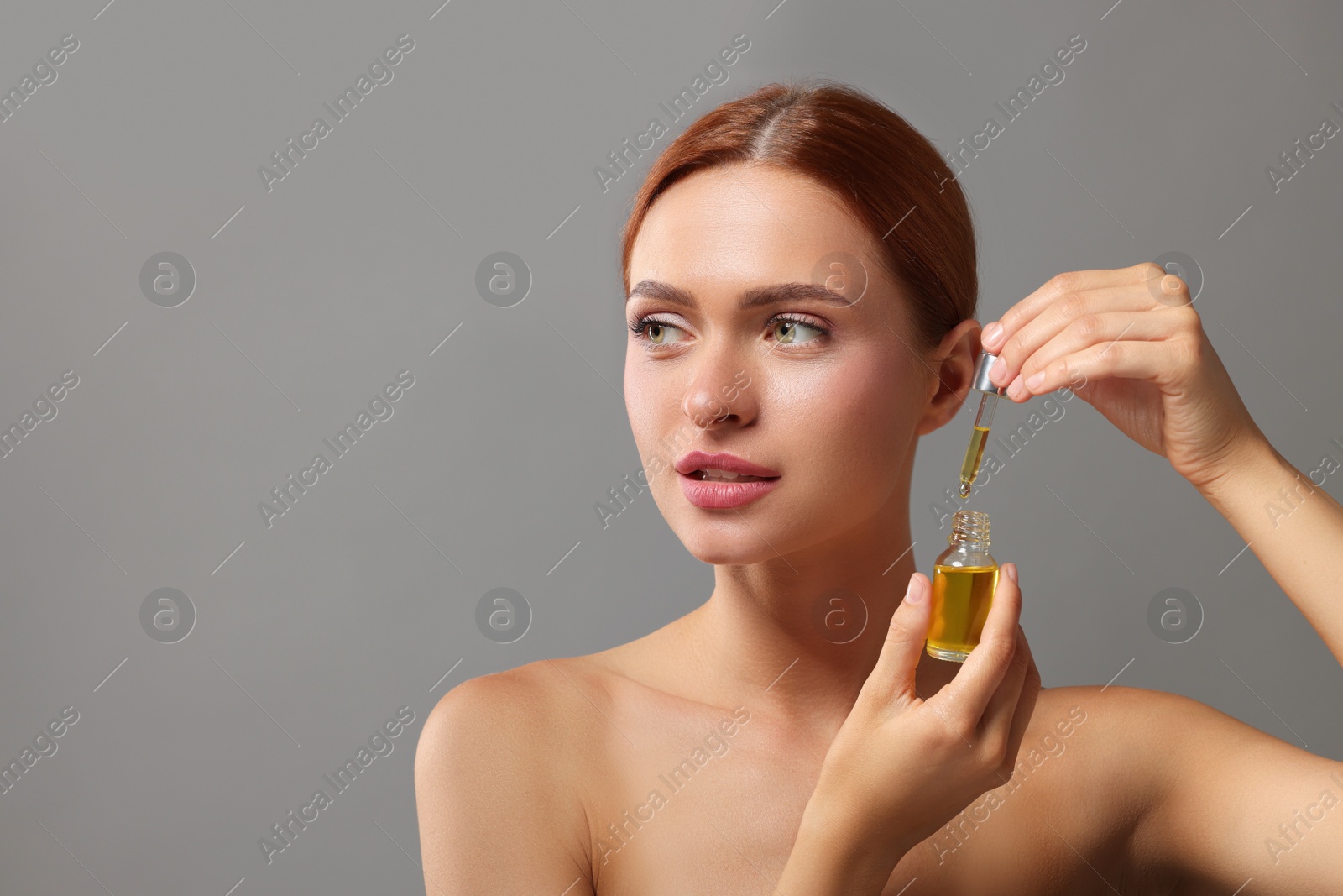 Photo of Beautiful young woman with bottle of cosmetic serum on grey background, space for text