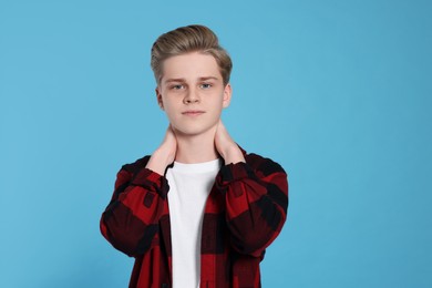Photo of Teenage boy suffering from pain in neck on light blue background. Arthritis symptom