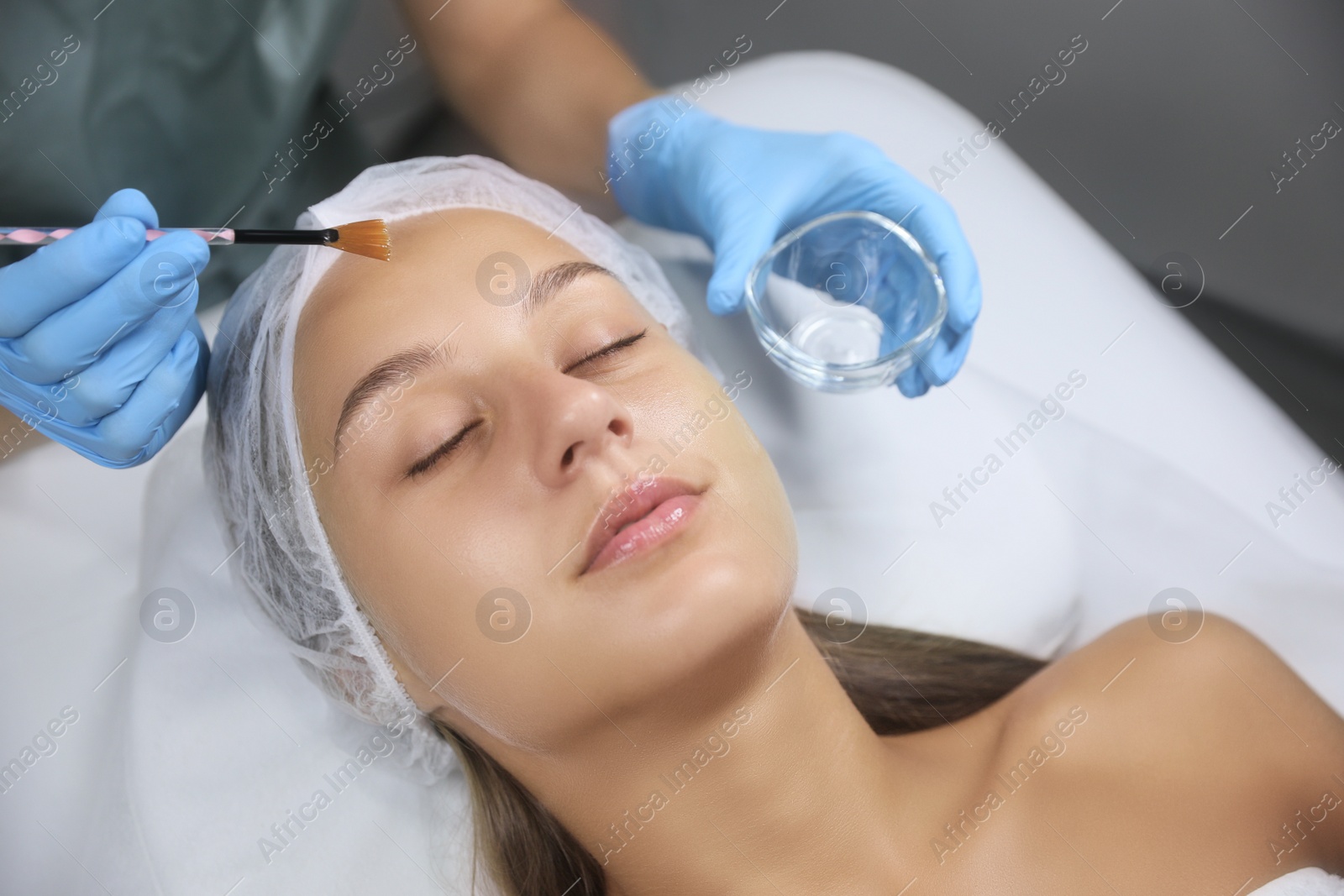 Photo of Cosmetologist applying chemical peel product on client's face in salon