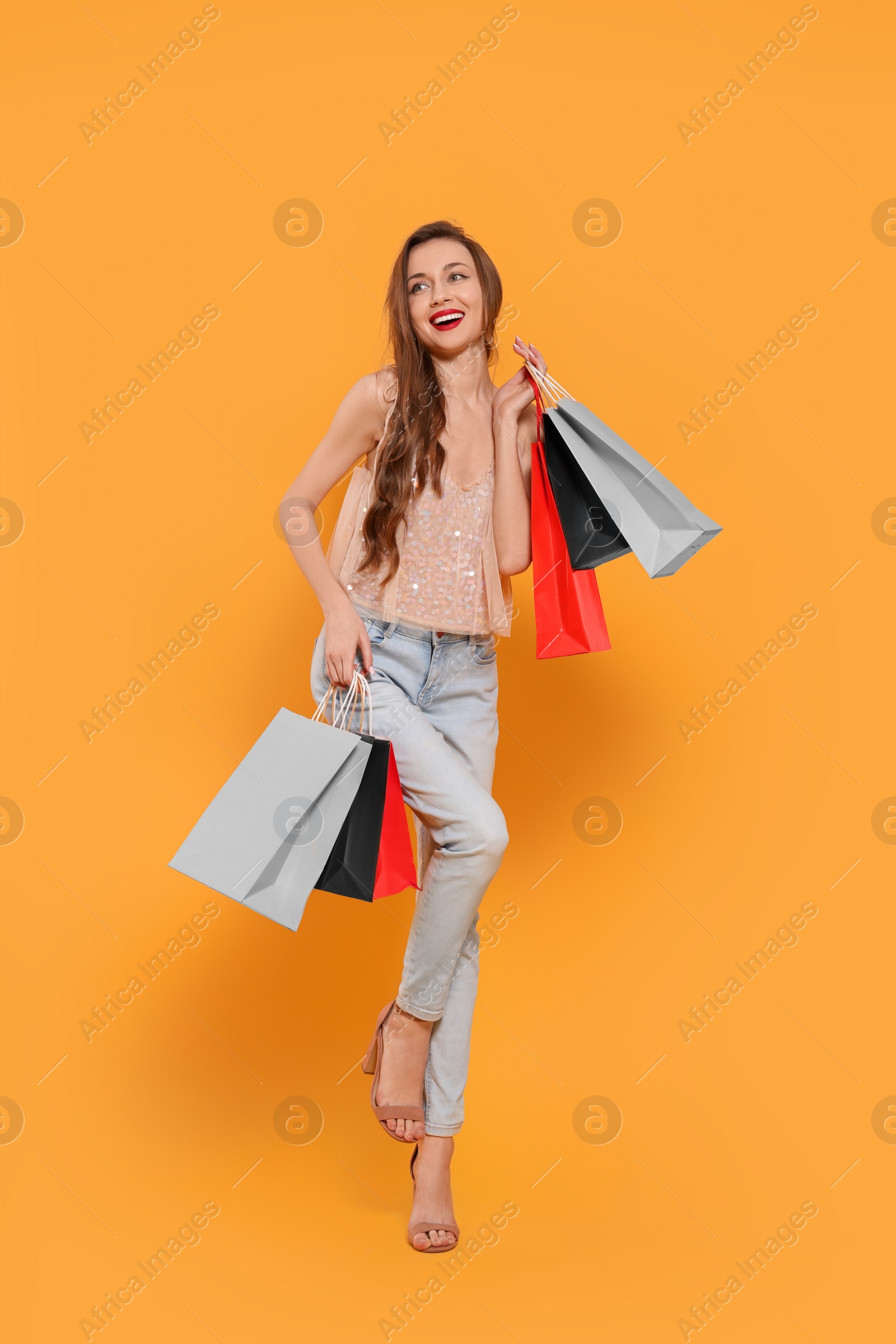 Photo of Stylish young woman with shopping bags on orange background