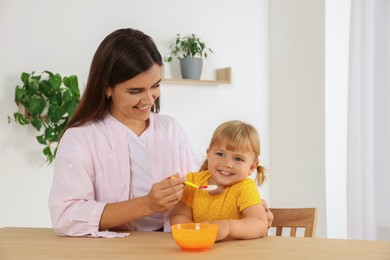 Mother feeding her cute little child with yogurt at wooden table indoors