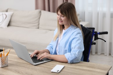 Woman in wheelchair using laptop at table in home office