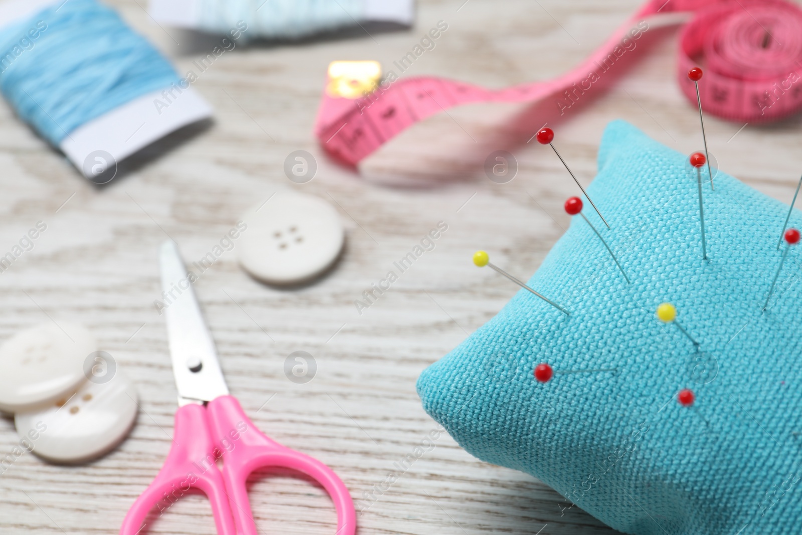 Photo of Light blue pincushion with pins and other sewing tools on wooden table, closeup