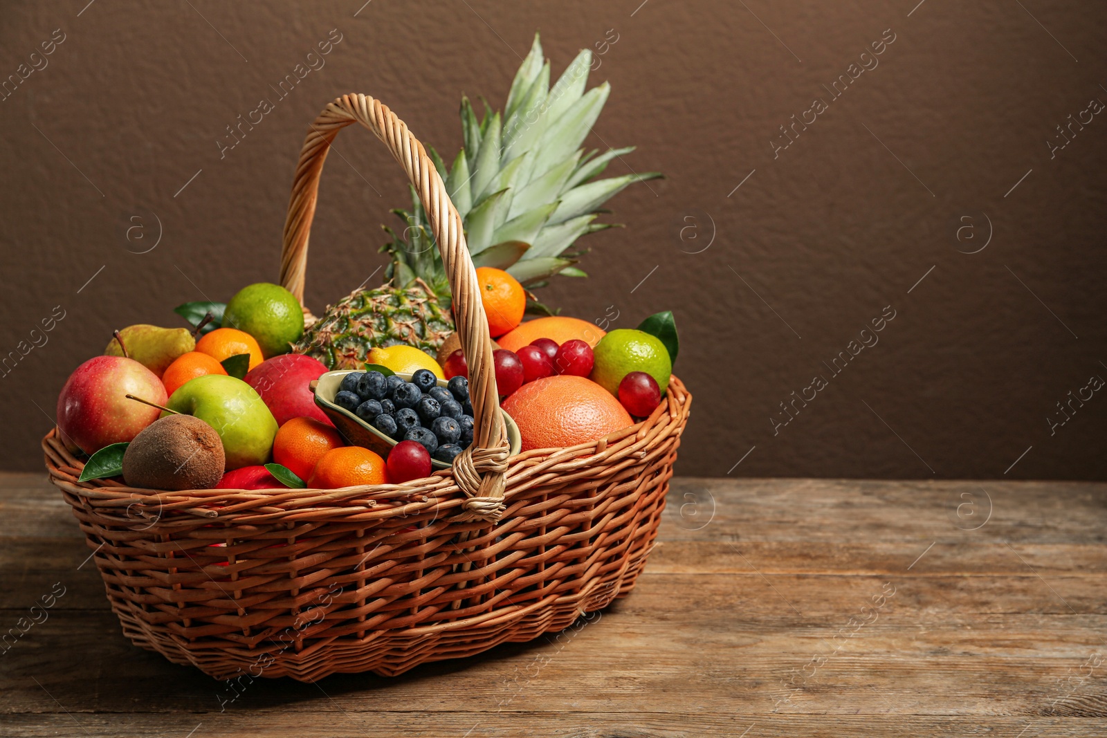 Photo of Assortment of fresh exotic fruits in wicker basket on wooden table. Space for text