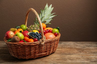 Assortment of fresh exotic fruits in wicker basket on wooden table. Space for text
