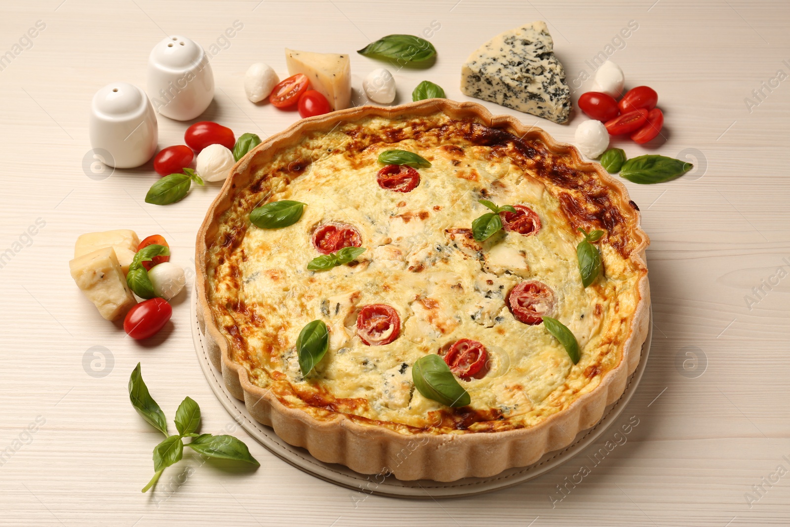 Photo of Delicious homemade cheese quiche and ingredients on wooden table