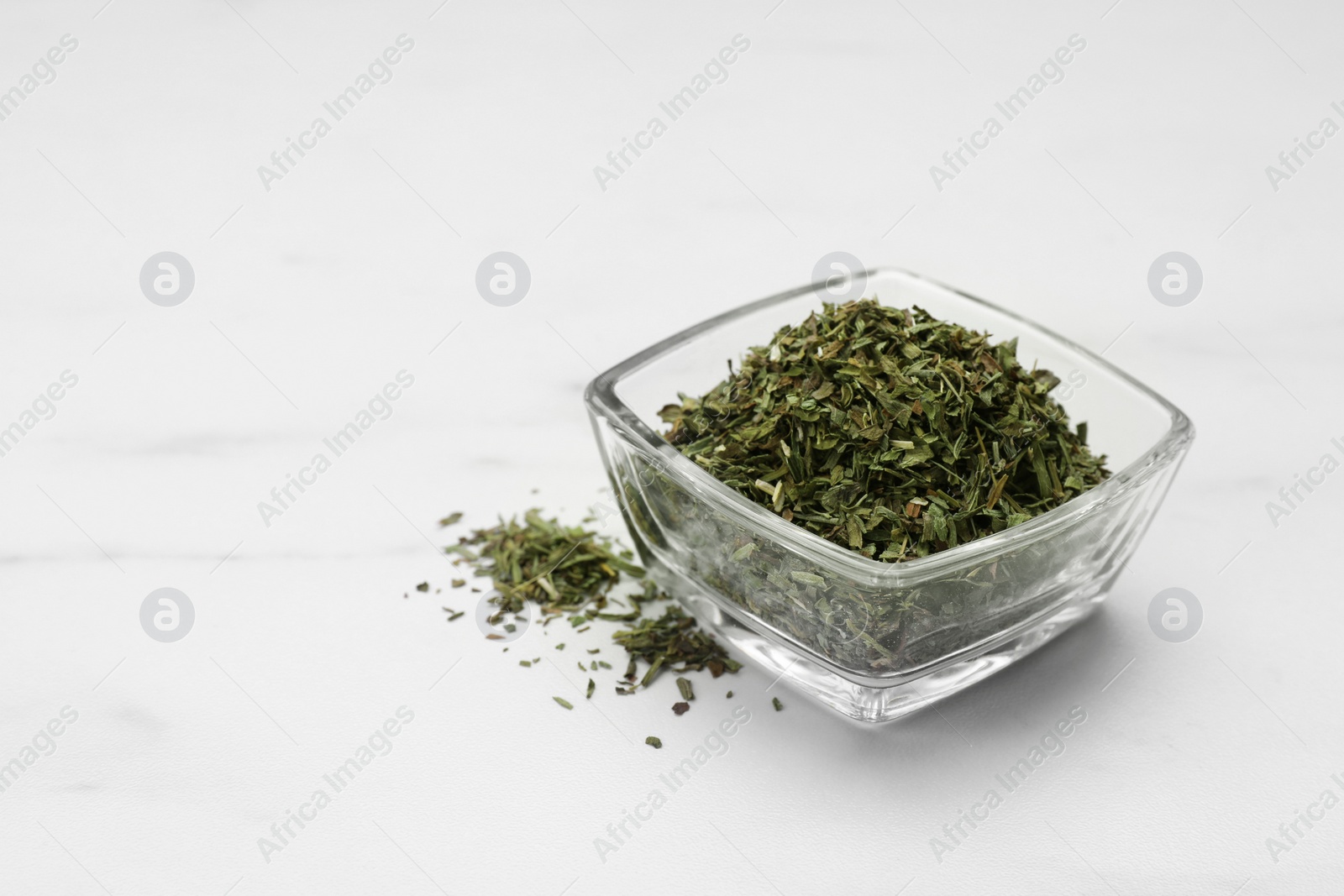 Photo of Dry tarragon in glass bowl on white table, space for text