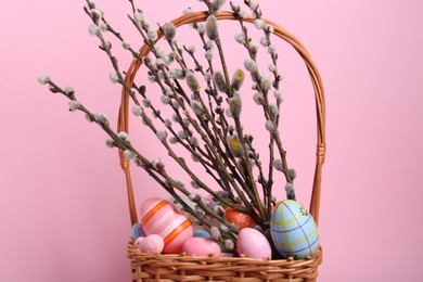 Wicker basket with beautiful willow branches and painted eggs on pink background. Easter decor