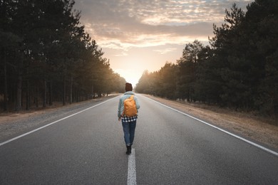 Woman with backpack going along road near forest, back view