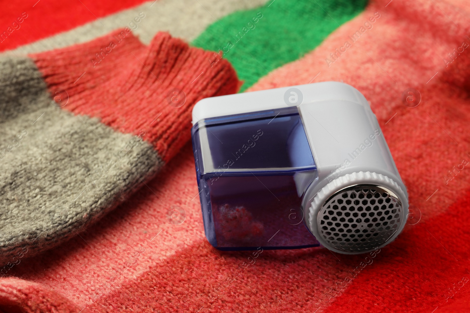 Photo of Modern fabric shaver on colorful knitted sweater, closeup