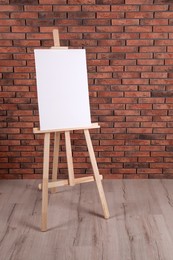 Photo of Wooden easel with blank canvas near brick wall