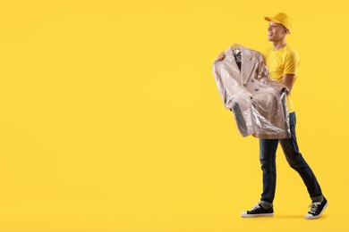 Dry-cleaning delivery. Happy courier holding coat in plastic bag on orange background, space for text