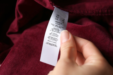 Photo of Woman reading clothing label with size and content information on red garment, closeup