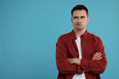 Photo of Resentful man with crossed arms on light blue background, space for text