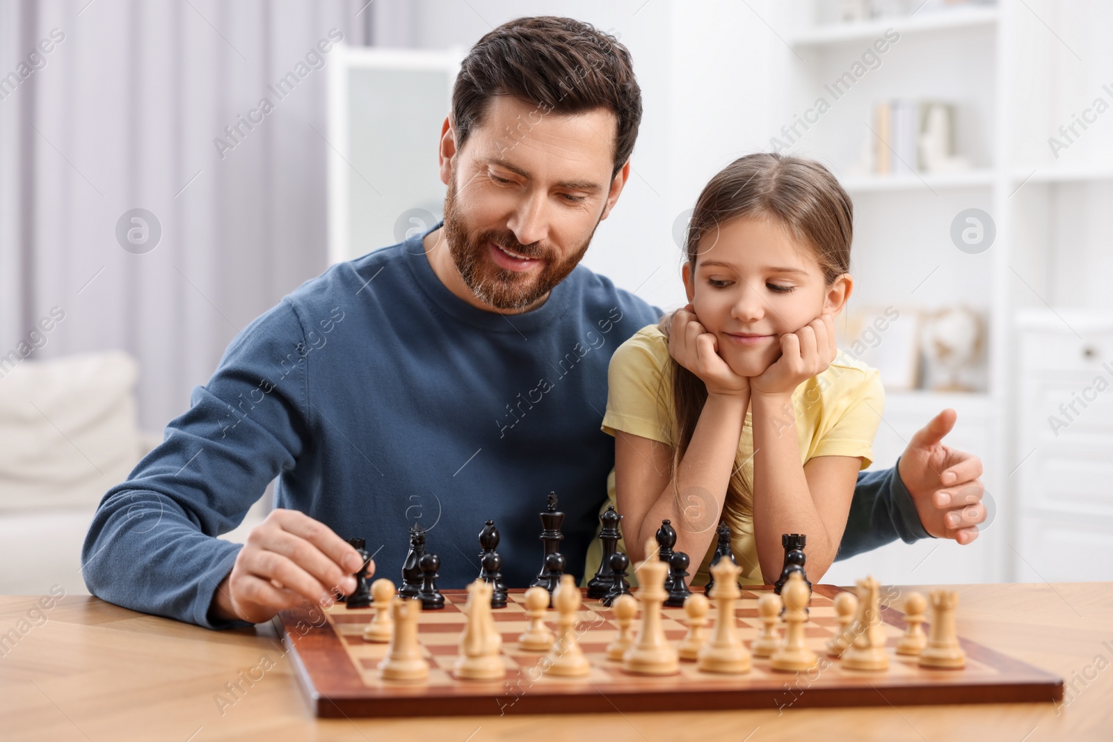 Photo of Father teaching his daughter to play chess at home