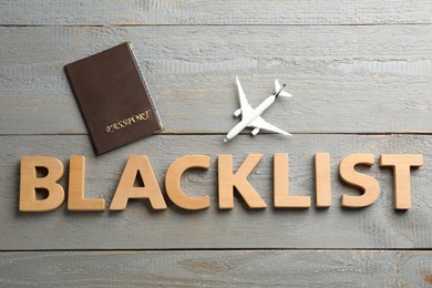 Word Blacklist of letters, toy airplane and passport on grey wooden background, flat lay