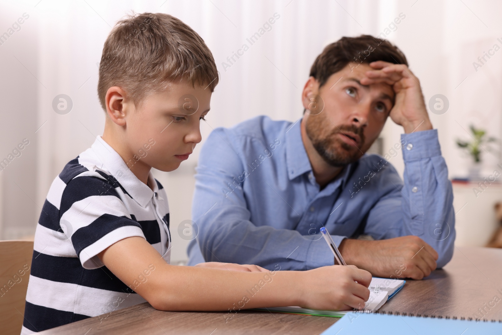 Photo of Dyslexia problem. Annoyed father helping son with homework at table indoors, selective focus