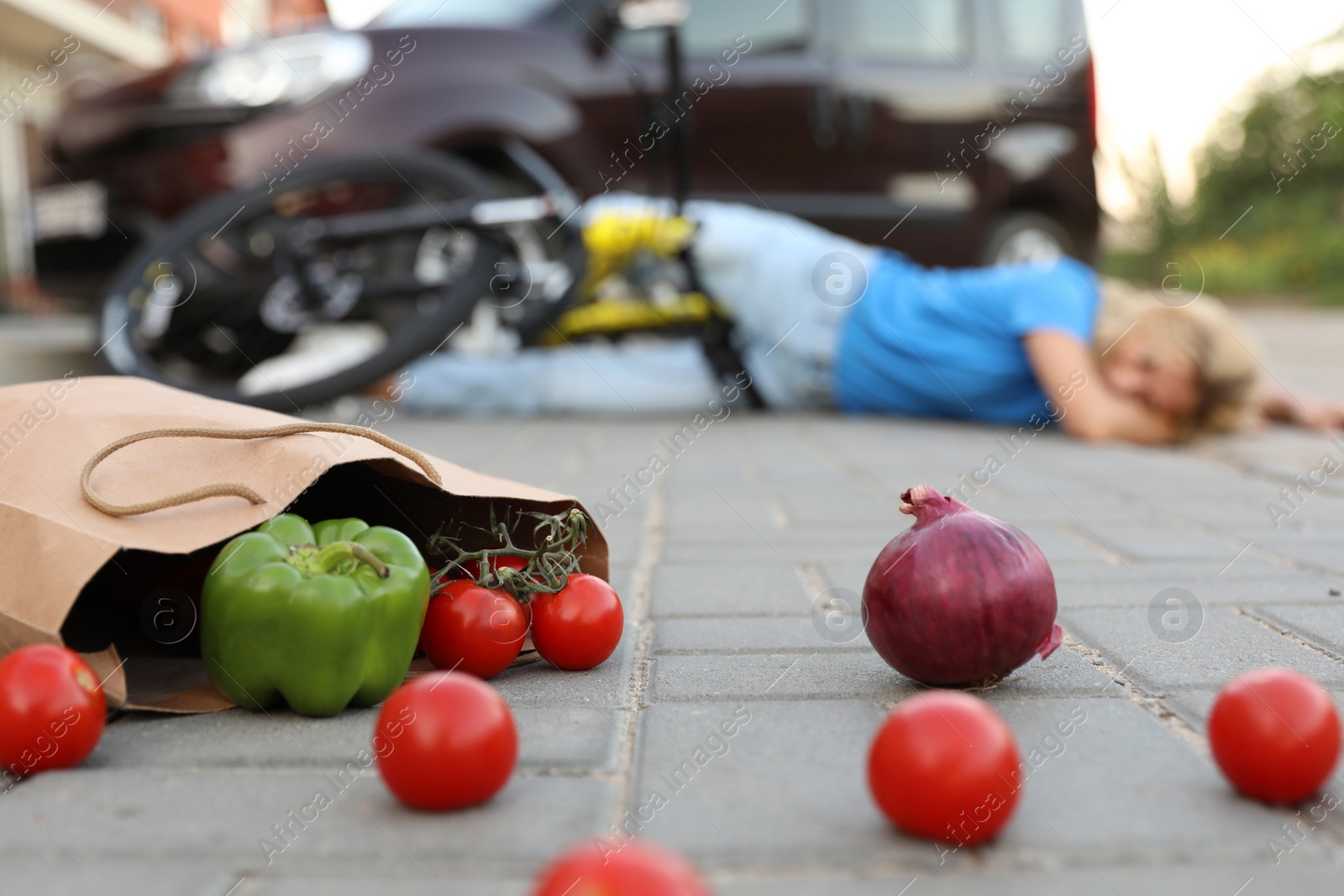 Photo of Woman fallen from bicycle after car accident outdoors, focus on scattered vegetables