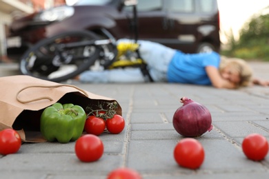 Photo of Woman fallen from bicycle after car accident outdoors, focus on scattered vegetables