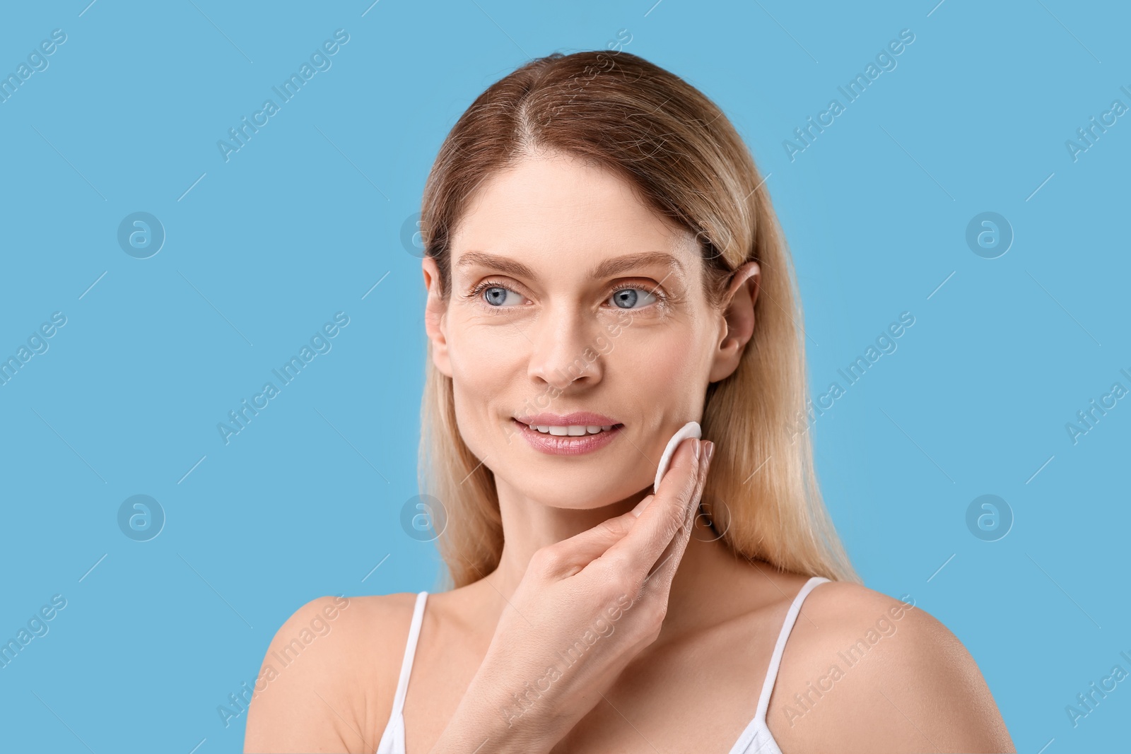 Photo of Beautiful woman removing makeup with cotton pad on light blue background