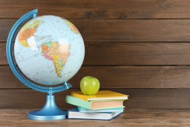 Photo of Globe, books and fresh apple on wooden table, space for text. Geography lesson