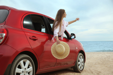 Photo of Happy woman leaning out of car window on beach. Summer vacation trip