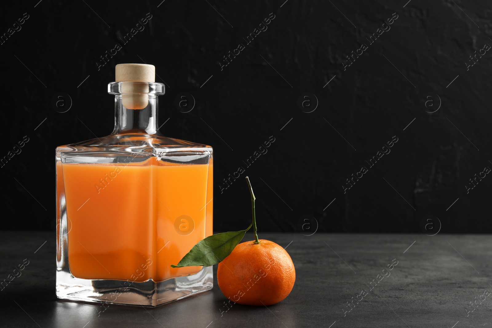 Photo of Delicious tangerine liqueur in glass bottle and fresh fruit on grey table, space for text