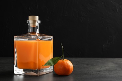 Photo of Delicious tangerine liqueur in glass bottle and fresh fruit on grey table, space for text