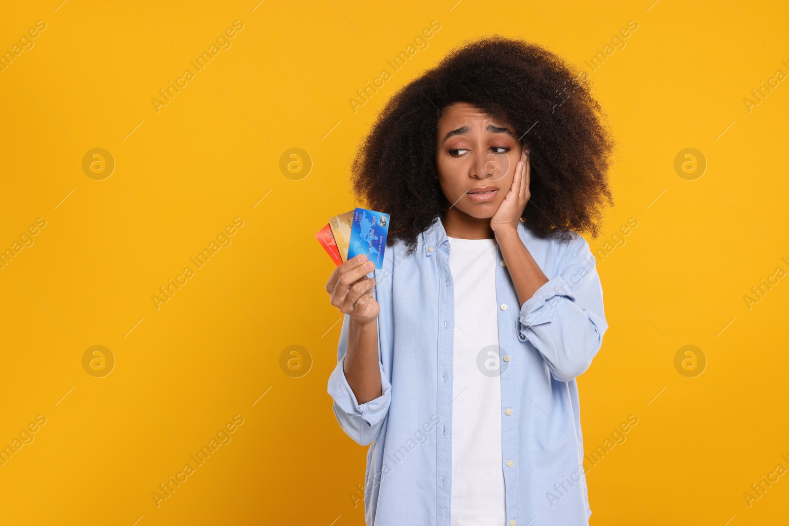 Photo of Confused woman with credit cards on orange background, space for text. Debt problem