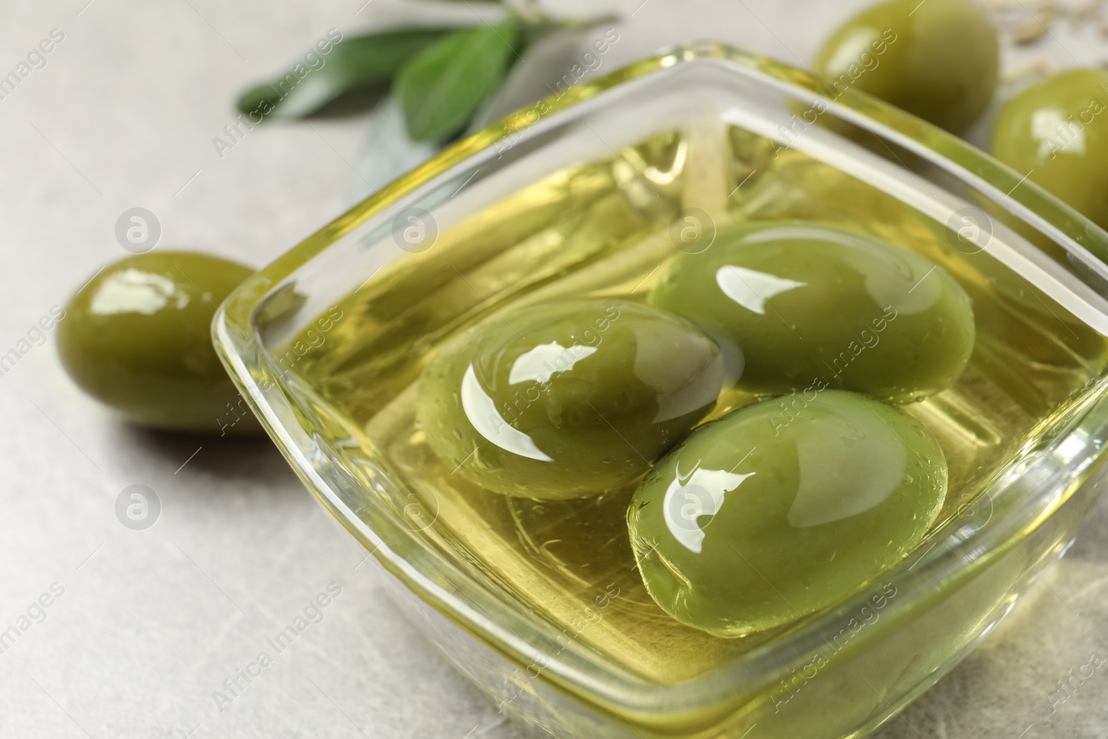 Photo of Glass bowl with fresh olive oil on light grey table, closeup