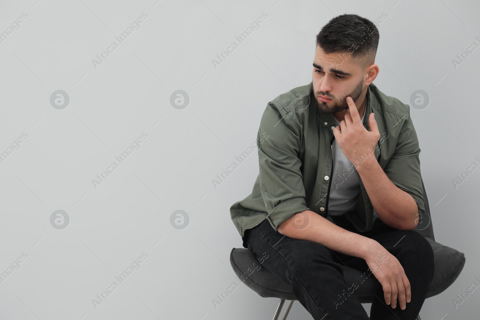 Photo of Sad man sitting near light grey wall. Space for text