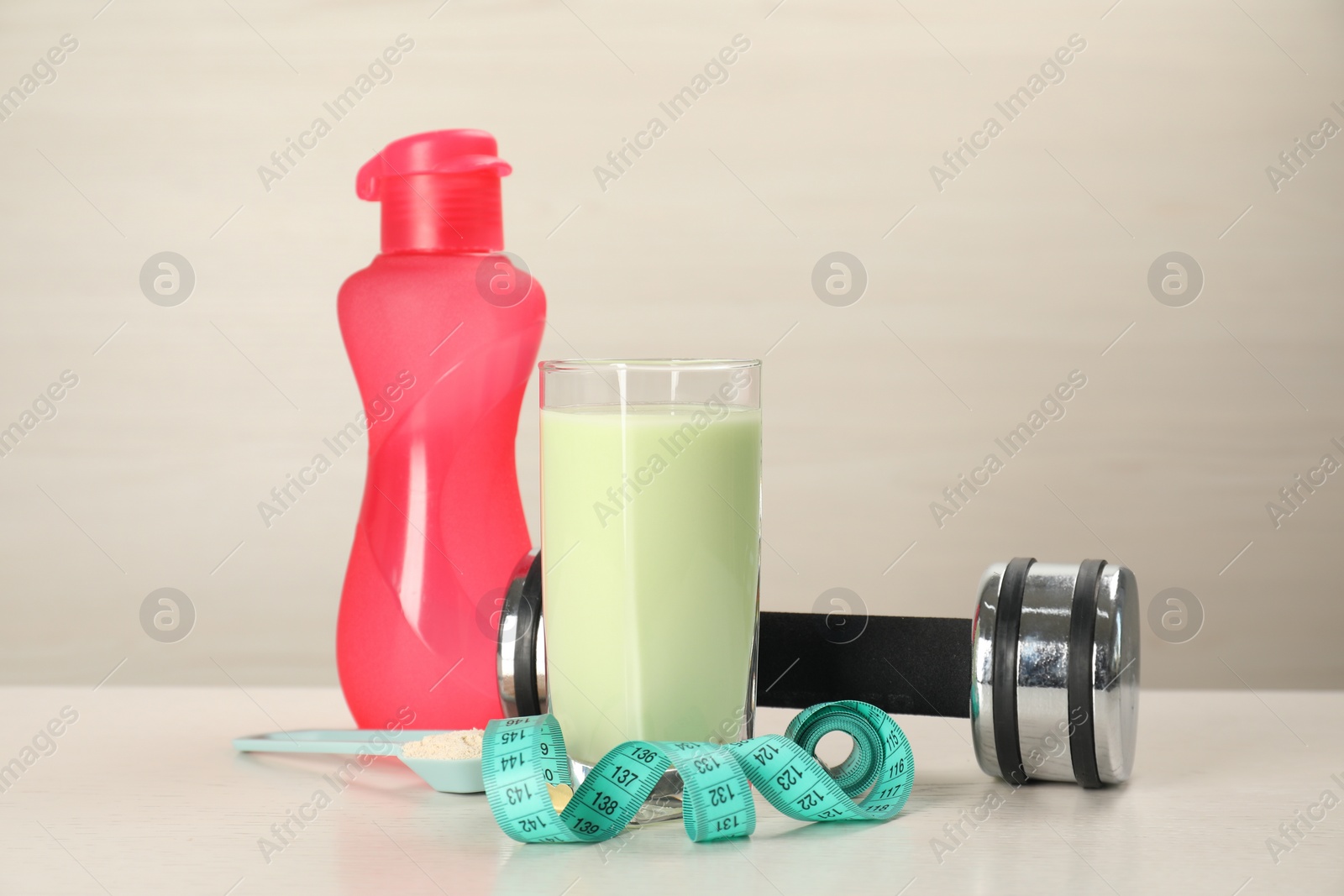 Photo of Tasty shake, bottle, dumbbell, measuring tape and powder on light table. Weight loss