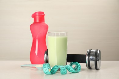 Photo of Tasty shake, bottle, dumbbell, measuring tape and powder on light table. Weight loss