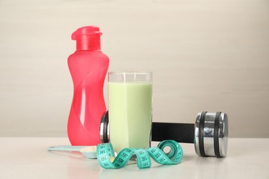 Tasty shake, bottle, dumbbell, measuring tape and powder on light table. Weight loss