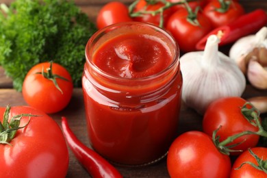 Photo of Jar of tasty ketchup and ingredients on wooden table, closeup