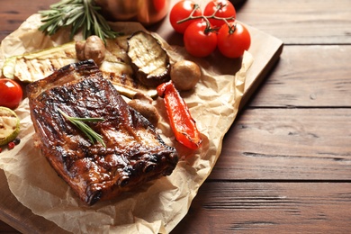 Photo of Delicious barbecued ribs served with vegetables on wooden table. Space for text