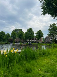 Photo of Beautiful view of city canal with pier and moored boat surrounded by greenery