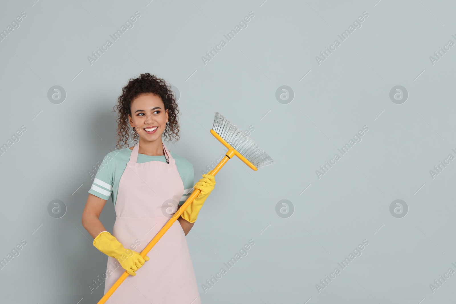 Photo of African American woman with yellow broom on grey background, space for text