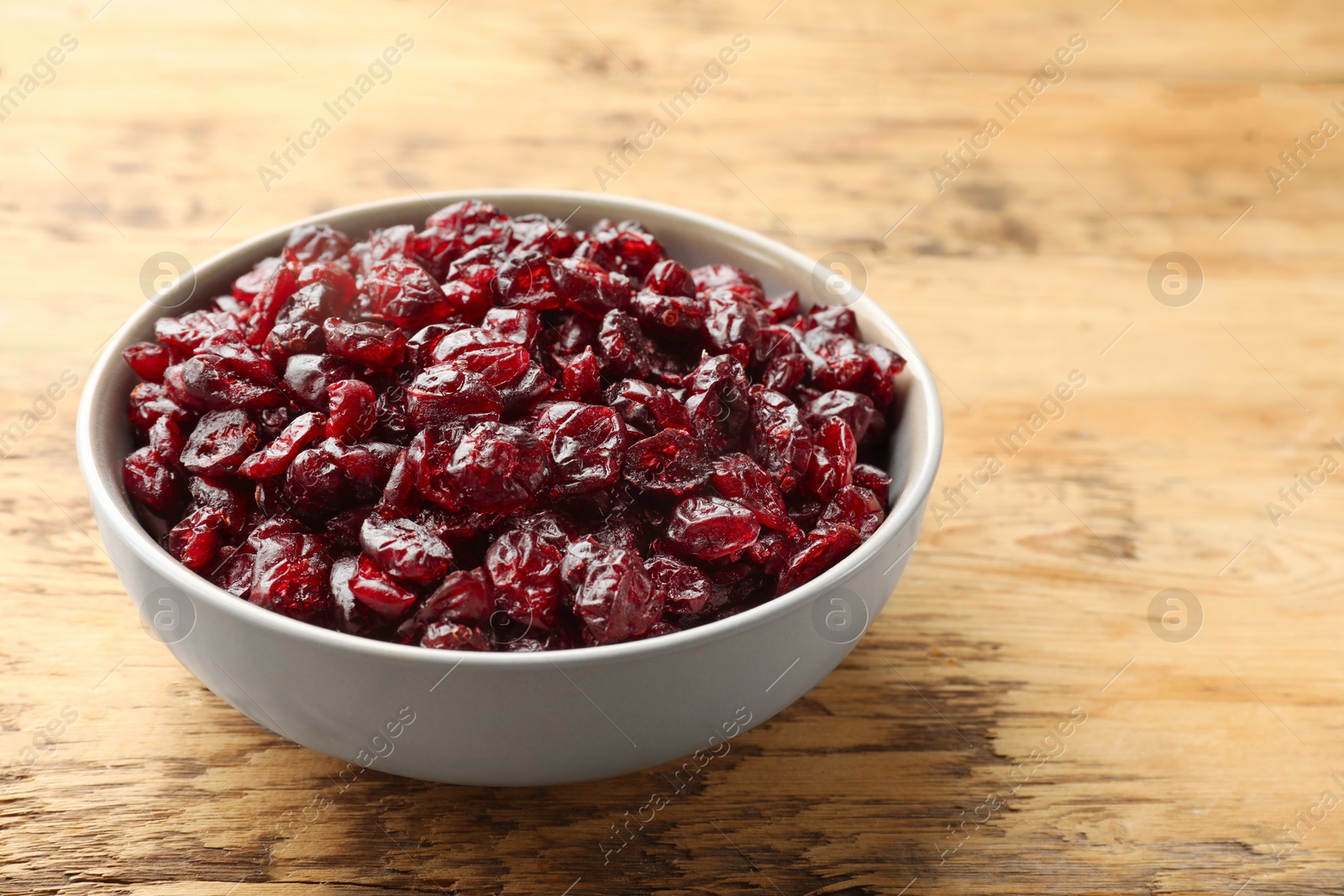 Photo of Tasty dried cranberries in bowl on wooden table, closeup