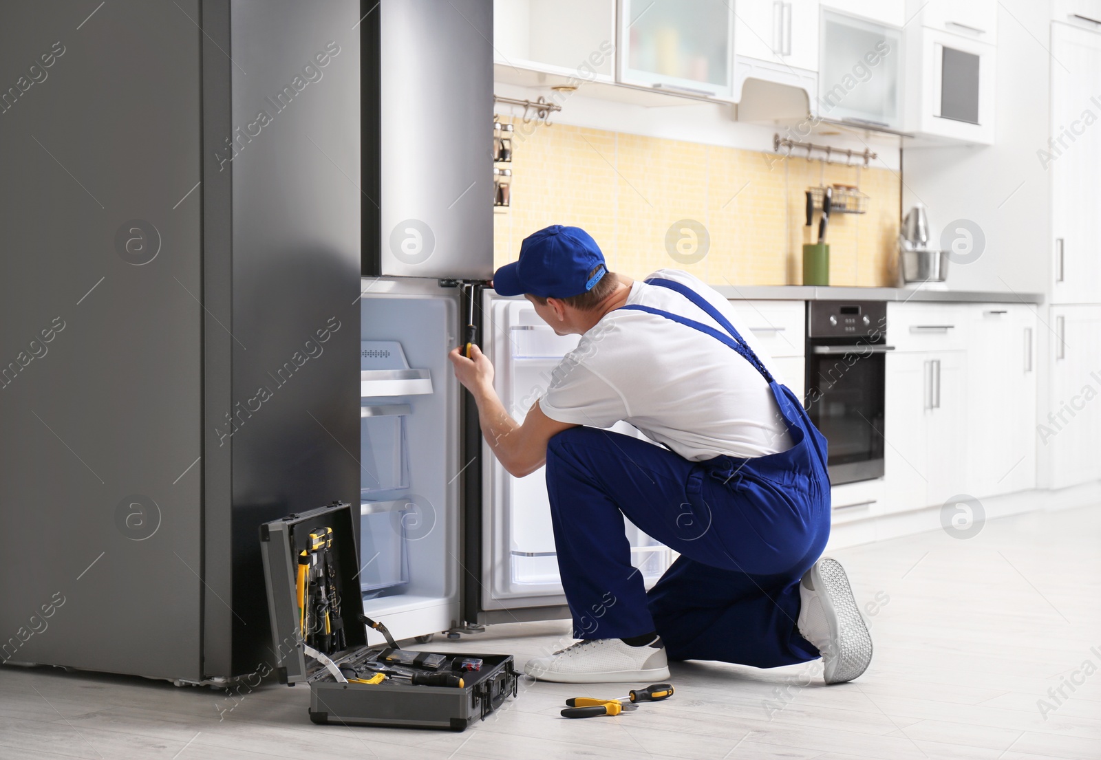 Photo of Male technician with screwdriver repairing refrigerator in kitchen