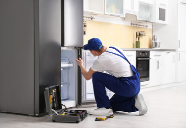 Male technician with screwdriver repairing refrigerator in kitchen