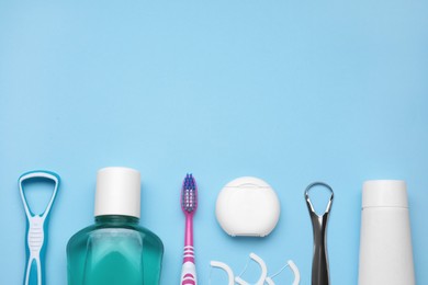 Photo of Tongue cleaners and other oral care products on light blue background, flat lay. Space for text