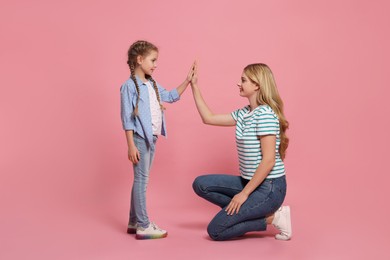 Photo of Mother and daughter giving high five on pink background