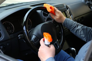 Man cleaning steering wheel with rag and spray bottle in car, closeup