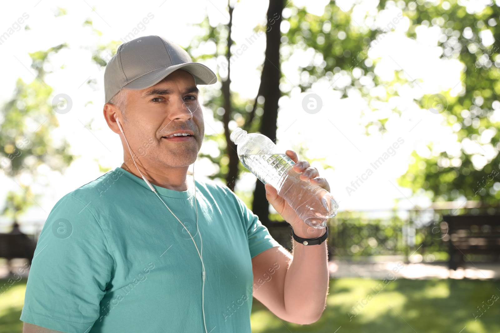 Photo of Handsome mature man with bottle of water in park, space for text. Healthy lifestyle